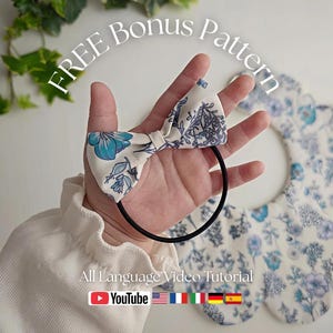 May include: A white and blue floral bow hair tie held in a hand, with a matching bib in the background. The image includes the text "FREE Bonus Pattern" and "All Language Video Tutorial" with a YouTube logo.