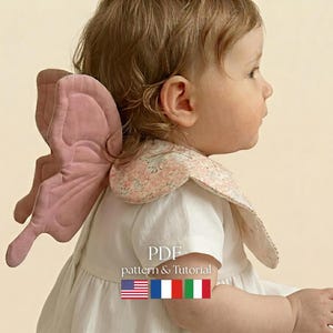 以下が含まれることがあります： 白いドレスを着た子供とピンクの蝶の羽のアクセサリー。 羽はドレスの背中に取り付けられています。 画像には「PDFパターンとチュートリアル」というテキストと、米国、フランス、イタリアの国旗が含まれています。