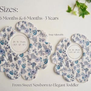 May include: Two floral baby bibs in different sizes, featuring a white background with blue and purple flower patterns. The bibs are snap adjustable and measure 9.5 to 13 inches in width. Text on the image reads "From Sweet Newborn to Elegant Toddler."