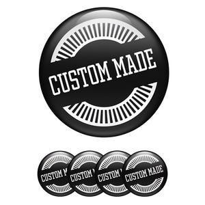 May include: A black button with the text "CUSTOM MADE" in white, surrounded by a white semi-circular design. Four smaller buttons with the same design are below the larger button. The buttons have a glossy finish.