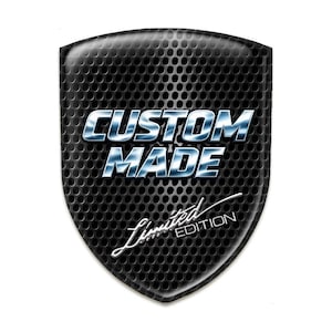 May include: A black shield-shaped emblem with a textured, perforated surface. The words "CUSTOM MADE" are in a metallic, blue-and-white font. Below, in a cursive font, is "Limited Edition".