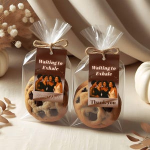 May include: Two clear cellophane bags tied with twine, each containing a large chocolate chip cookie. Each bag has a brown tag with the text "Waiting to Exhale" and an image of four women. One tag says "Ladies Night" and the other says "Thank you."