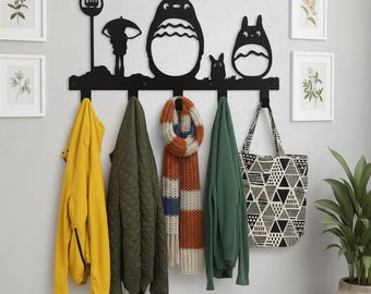 May include: Black metal wall-mounted coat rack featuring a silhouette design of characters from a popular animated film. The rack holds a yellow jacket, green quilted jacket, striped scarf, green sweater, and a tote bag with a geometric pattern.