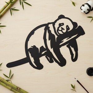 Op de afbeelding: Een zwarte metalen wanddecoratie uitgesneden in de vorm van een panda die zijn kop op een bamboestengel laat rusten. Het ontwerp heeft gedurfde, strakke lijnen en een plat silhouet, waarbij de panda in een ontspannen, liggende houding is afgebeeld.