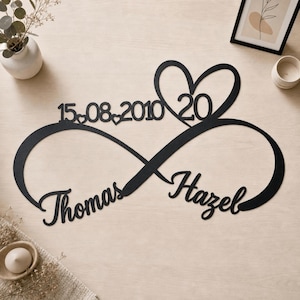 May include: A black metal wall sign shaped like an infinity symbol featuring the names Thomas and Hazel in cursive script, the date 15.08.2010 with small heart accents, and a large heart outline containing the number 20 at the top center.