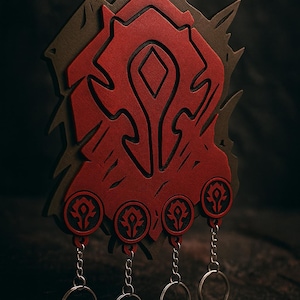 May include: A layered, red and brown decorative emblem with four keychains. The emblem features a stylized design with a diamond shape in the centre. The keychains have silver rings.