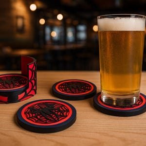 May include: A pint of beer rests on a black, red, and blue spiderweb-themed coaster. The coaster set includes a holder and two additional coasters. The coasters are on a wooden surface.