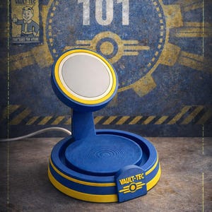 May include: A blue and yellow Vault-Tec wireless charger. The charger features a circular charging pad with a white centre, supported by a curved stand. The base has the Vault-Tec logo. The background displays the number 101 and Vault-Tec branding.
