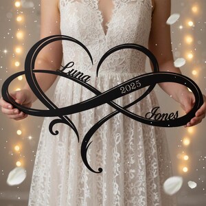 May include: A black metal wall sign featuring an intertwined heart and infinity symbol design. The cutout text reads Luna, 2025, and Jones. The sign has a smooth finish and is held horizontally, showcasing a decorative script font for the names.