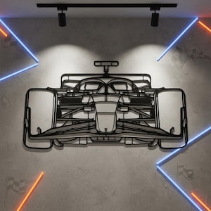 May include: A black metal Formula 1 race car wall art piece. The artwork is mounted on a gray wall and is illuminated by overhead spotlights and neon lights in blue and orange. The design is a detailed outline of a race car.