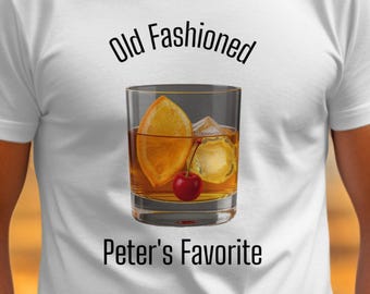 May include: White t-shirt with a graphic of an Old Fashioned cocktail, including a lemon peel, ice, and cherry. The text above the graphic reads "Old Fashioned," and below it, "Peter's Favorite."