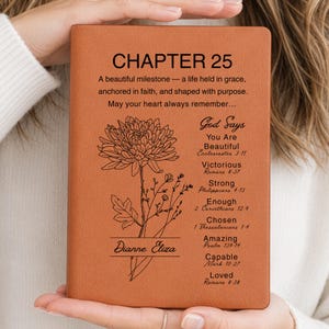 May include: A tan leather-bound journal with the text "CHAPTER 25" and inspirational quotes. A floral illustration and the name "Dianne Eliza" are also featured. The journal is held by a person.