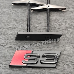 May include: Two metal toggle bolts with black mounting plates and a black and red S3 emblem. The emblem has a black border and the text "S3" in a metallic finish. The background is a grey textured surface.