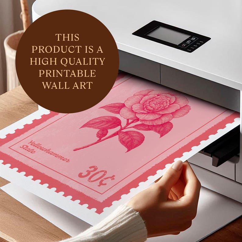 May include: A pink floral print wall art is being printed from a printer. The art features a detailed illustration of a camellia flower and leaves, set against a light pink background. The print has a postage stamp design with the text "Yellowhammer State" and "30&cent;".