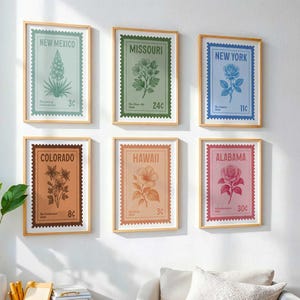 May include: Six framed botanical prints resembling vintage postage stamps. Each print features a state name, a floral illustration, and a price. The color palette includes shades of green, blue, orange, and pink, with wooden frames.