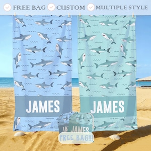 May include: Two beach towels with shark patterns, one light blue and one teal, hanging on a clothesline. Each towel has the name "JAMES" printed on it. A matching drawstring bag is in front of the towels, with the text "ID JAMES FREE BAG!!!".