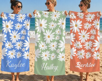 May include: Three rectangular beach towels featuring a white daisy pattern with yellow centers. The blue towel displays the name Kaylee, the green towel displays the name Hailey, and the orange towel displays the name Berklee in white script.