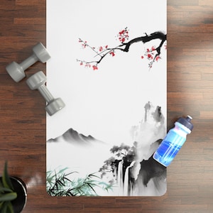 May include: White yoga mat with a black and white Asian-inspired landscape design. The design features a mountain range, waterfall, and bamboo. A branch with red flowers is at the top. A blue water bottle and two gray dumbbells are on the side.