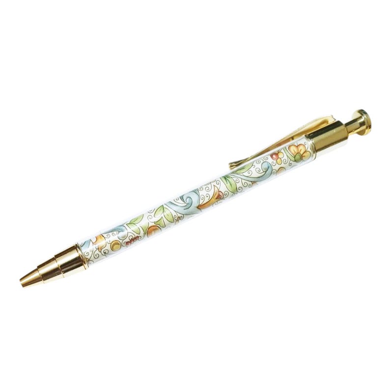 May include: A decorative pen with a gold-colored tip, clip, and end. The pen's barrel is white with a colorful floral design in green, blue, orange, and yellow. The pen is a writing instrument.