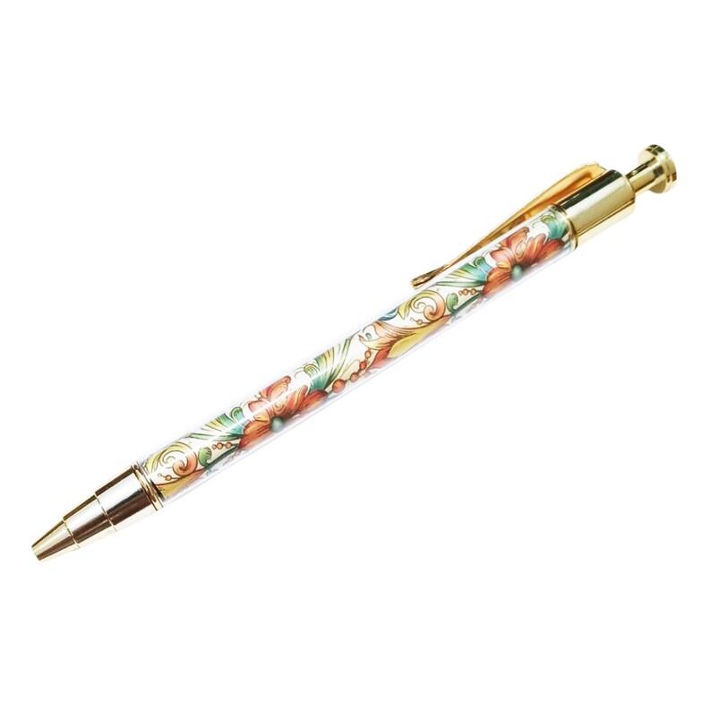 May include: A gold-toned pen with a floral design. The pen's barrel features a white background with red, orange, and green flowers. The pen has a gold clip and tip, and is designed for writing.
