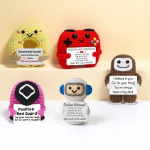 Peut inclure: Ensemble de figurines crochetées : un donut jaune, une manette de jeu rouge, un singe marron, un garde rose et un astronaute blanc. Chacun tient une pancarte avec des messages positifs. Les figurines sont faites à la main.
