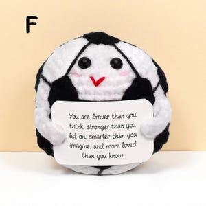May include: A handmade, plush soccer ball with a smiling face and a message. The black and white ball holds a white card with the text: "You are braver than you think, stronger than you let on..."