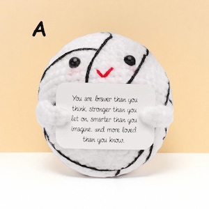 May include: A white crocheted ball with black accents and a smiling face holds a white card with text. The card reads: "You are braver than you think, stronger than you let on, smarter than you imagine, and more loved than you know."