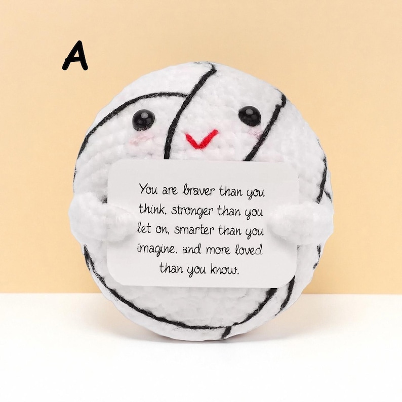 May include: A white crocheted ball with black accents and a smiling face holds a white card with text. The card reads: "You are braver than you think, stronger than you let on, smarter than you imagine, and more loved than you know."