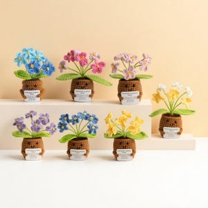 May include: A collection of handmade crochet plants in various colors, including blue, pink, purple, and yellow. Each plant features a smiling pot with a small tag that reads "Emotional Support Plant". The flowers have green leaves.