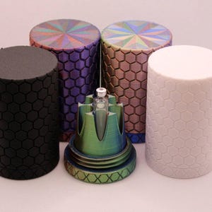 Peut inclure: Plusieurs objets cylindriques avec un motif en nid d'abeille. Les objets sont de différentes couleurs, dont le noir, le violet et le blanc. Un objet central multicolore avec un design complexe est également présent.