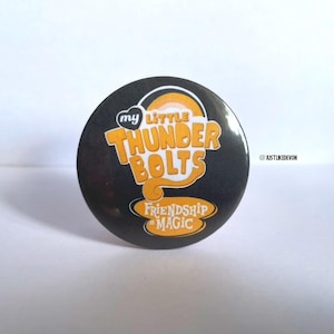 May include: A circular black badge featuring the words "my LITTLE THUNDERBOLTS" in orange and white, with a rainbow design. The text "FRIENDSHIP IS MAGIC" is in a curved banner at the bottom.