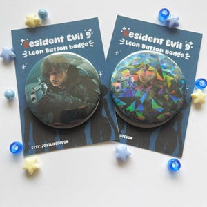 Op de afbeelding: Twee ronde button badges met Leon uit Resident Evil 9, gepresenteerd op donkerblauwe achtergrondkaarten met de tekst Resident Evil 9 Leon Button badge. Eén badge heeft een standaard afwerking, terwijl de andere een holografische geometrische overlay heeft.
