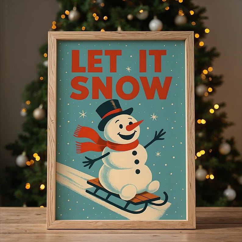 May include: A framed print with a winter theme. The artwork features a snowman wearing a black top hat and a red scarf, riding a sled down a snowy hill. The words "LET IT SNOW" are in red letters against a teal background.