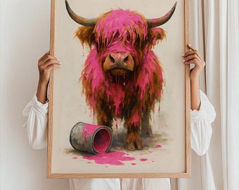 May include: A framed art print featuring a Highland cow covered in pink paint. The cow has brown fur and large horns. A spilled paint can is on the ground. The artwork is held by a person.