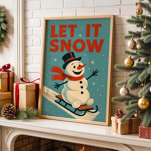 May include: A framed print featuring a snowman on a sled, with the words "LET IT SNOW" in red. The snowman is wearing a black top hat and a red scarf. The print is on a white mantelpiece with Christmas decorations.
