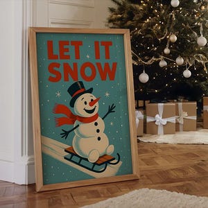 May include: A framed print with a vintage illustration of a snowman on a sled. The snowman wears a black top hat and a red scarf. The words "LET IT SNOW" are in red on a teal background. The frame is made of light wood. The print is displayed near a Christmas tree.