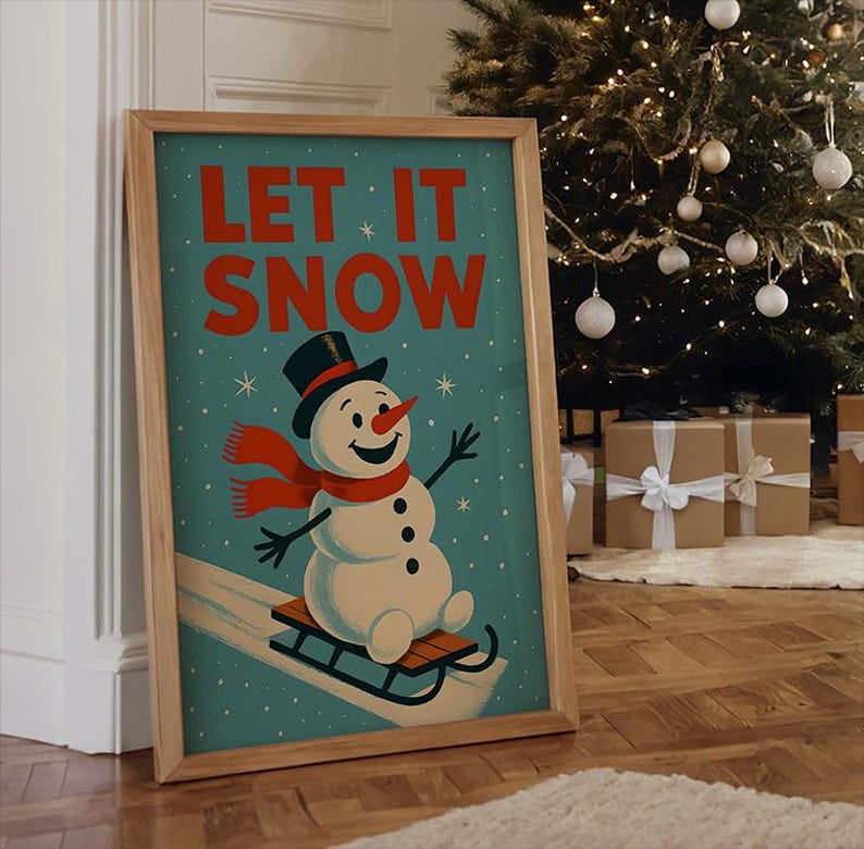 May include: A framed print with a vintage illustration of a snowman on a sled. The snowman wears a black top hat and a red scarf. The words "LET IT SNOW" are in red on a teal background. The frame is made of light wood. The print is displayed near a Christmas tree.
