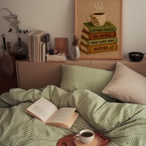 May include: A bedroom scene featuring a green and white gingham duvet and pillow set. An open book, a coffee cup on a wooden tray, and a framed picture of books and a coffee cup create a relaxing atmosphere. A stack of books and a vase are on the shelf.