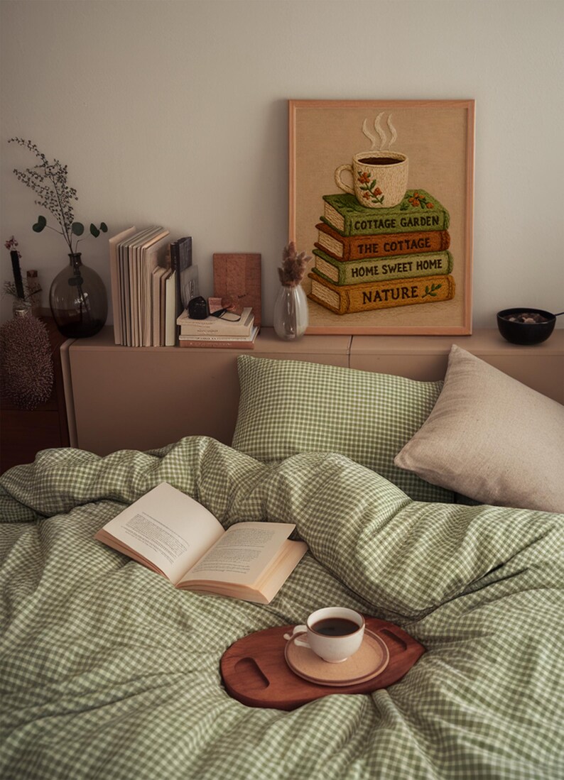 May include: A bedroom scene featuring a green and white gingham duvet and pillow set. An open book, a coffee cup on a wooden tray, and a framed picture of books and a coffee cup create a relaxing atmosphere. A stack of books and a vase are on the shelf.