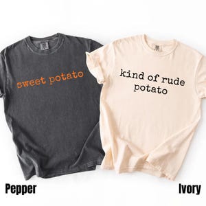 Könnte beinhalten: Zwei kurzärmelige T-Shirts. Eines ist dunkelgrau mit den Worten "sweet potato" in Orange. Das andere ist elfenbeinfarben mit den Worten "kind of rude potato" in Schwarz. Die Farben der Shirts sind unten mit "Pepper" und "Ivory" beschriftet.