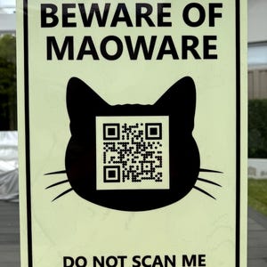 May include: A rectangular sign with a black border and a pale green background. The sign has the text "BEWARE OF MAOWARE" above a black cat silhouette with a QR code. Below the cat is the text "DO NOT SCAN ME".