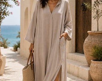 May include: A beige hooded kaftan dress featuring long sleeves, a deep V-neckline, and a side slit. The garment includes side pockets and is paired with a woven straw tote bag and brown sandals. The text Shahig Fabric Fusion is visible.