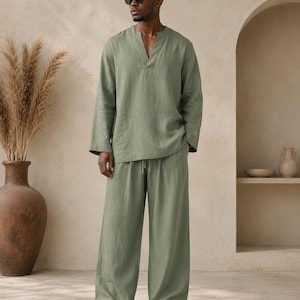May include: A sage green long-sleeved shirt with a V-neckline and matching wide-leg trousers featuring an elasticized drawstring waistband. The set is made of a solid-colored fabric and is worn with black sandals and dark-tinted sunglasses.