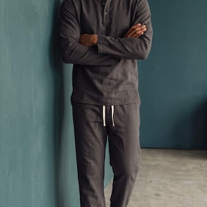 Könnte beinhalten: Ein dunkelgraues, langärmeliges Henley-Shirt mit Knopfleiste und eine dazu passende Hose mit Kordelzug. Das Set besteht aus strukturiertem Stoff und wird mit weißen Sneakern kombiniert. Der Text Shahig Fabric Fusion ist deutlich zu sehen.