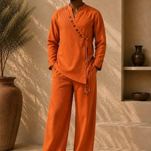 May include: A vibrant orange long-sleeved tunic featuring a diagonal button placket with dark circular buttons and a side tie closure, paired with matching wide-leg trousers. The ensemble is completed by dark brown slide sandals and sunglasses.