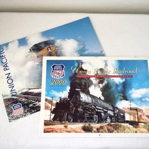 May include: A 2000 Union Pacific Railroad calendar featuring a black steam locomotive with a plume of smoke. The calendar is titled "A Century of Railroading 1880-2000".