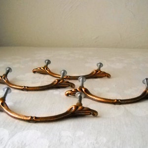 May include: Four antique-style cabinet pulls with a curved, ornate design. The pulls are made of a brass-colored metal with a silver-toned screw.