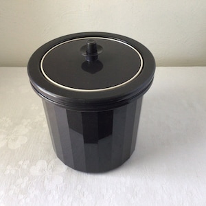 May include: A black plastic ice bucket with a lid and a small knob on top. The bucket has vertical ridges.