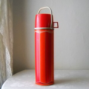 May include: Orange and white thermos with a geometric pattern and a white handle.