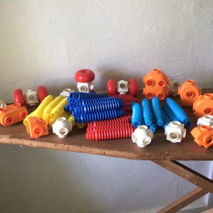 May include: A collection of plastic construction toy pieces including white, orange, and red multi-sided connectors, along with flexible ribbed tubes in yellow, blue, and red colors. The set features various geometric shapes and modular parts.